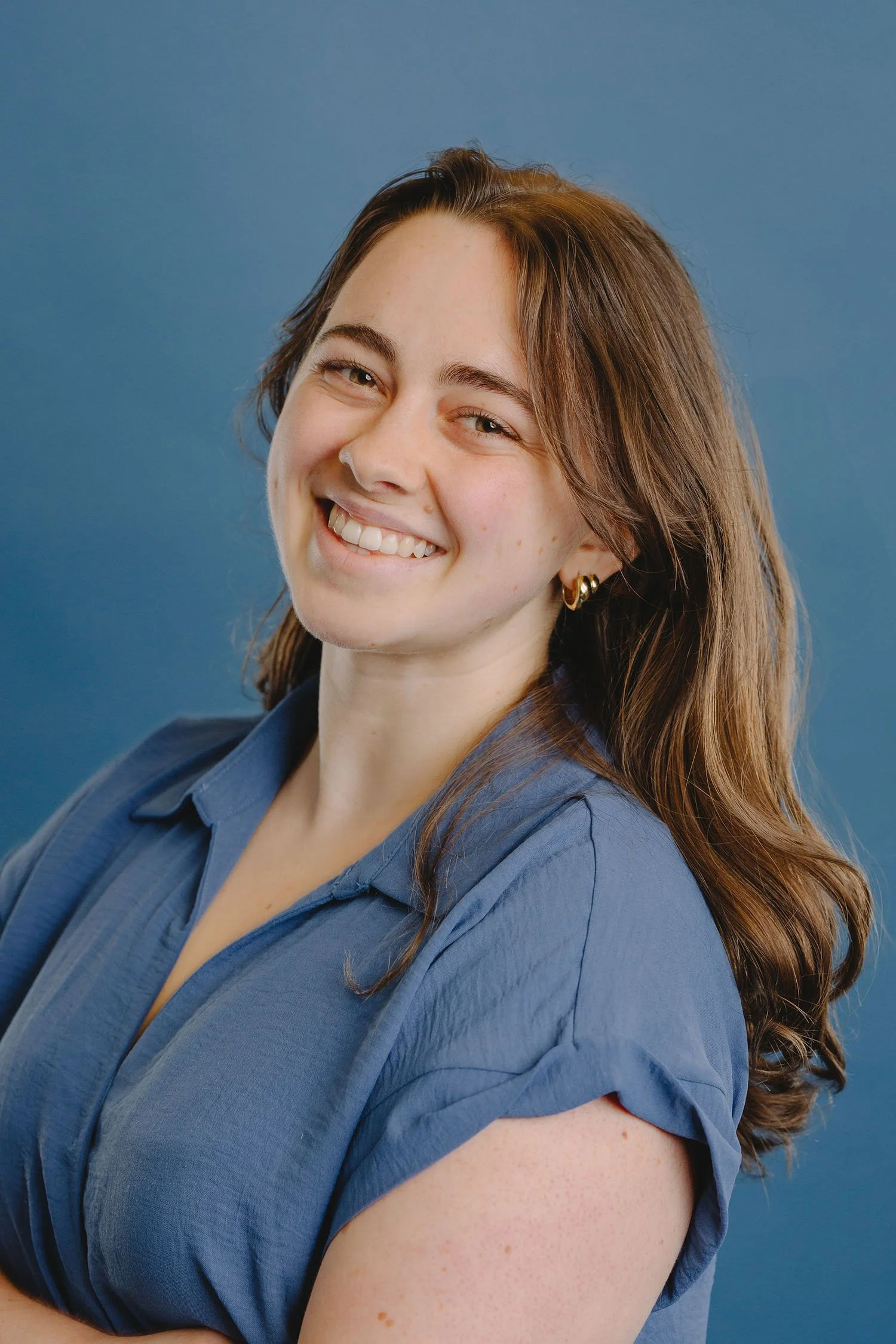 Smiling woman with brown hair, wearing a blue shirt, against a blue background.