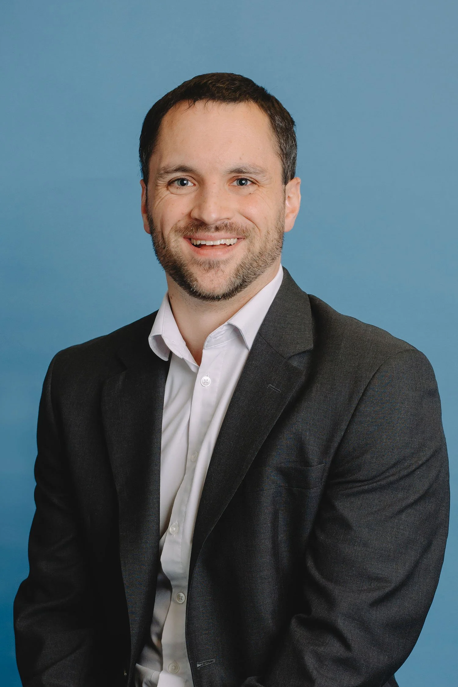 A smiling man in a suit posing against a blue background.
