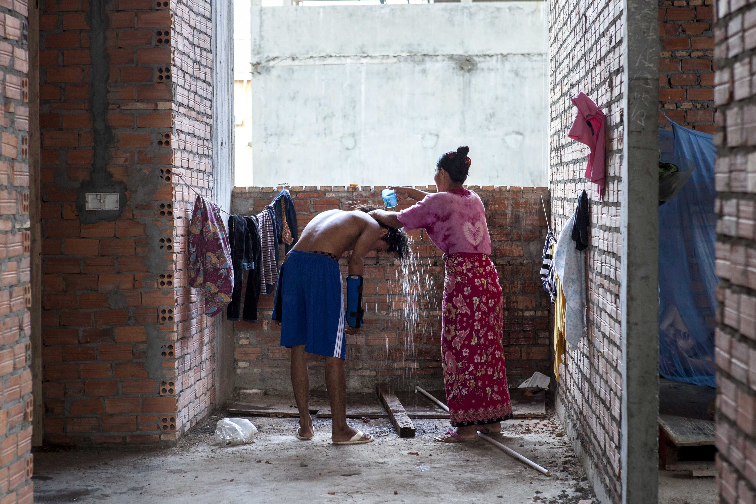  Orn Na, age 40, helps her son Vibol to wash his hair, after a multi-storey fall broke both his arms. Orn Na earns just over $6 a day cementing walls, yet remains stoic that the family can recover from the loss of their savings. 