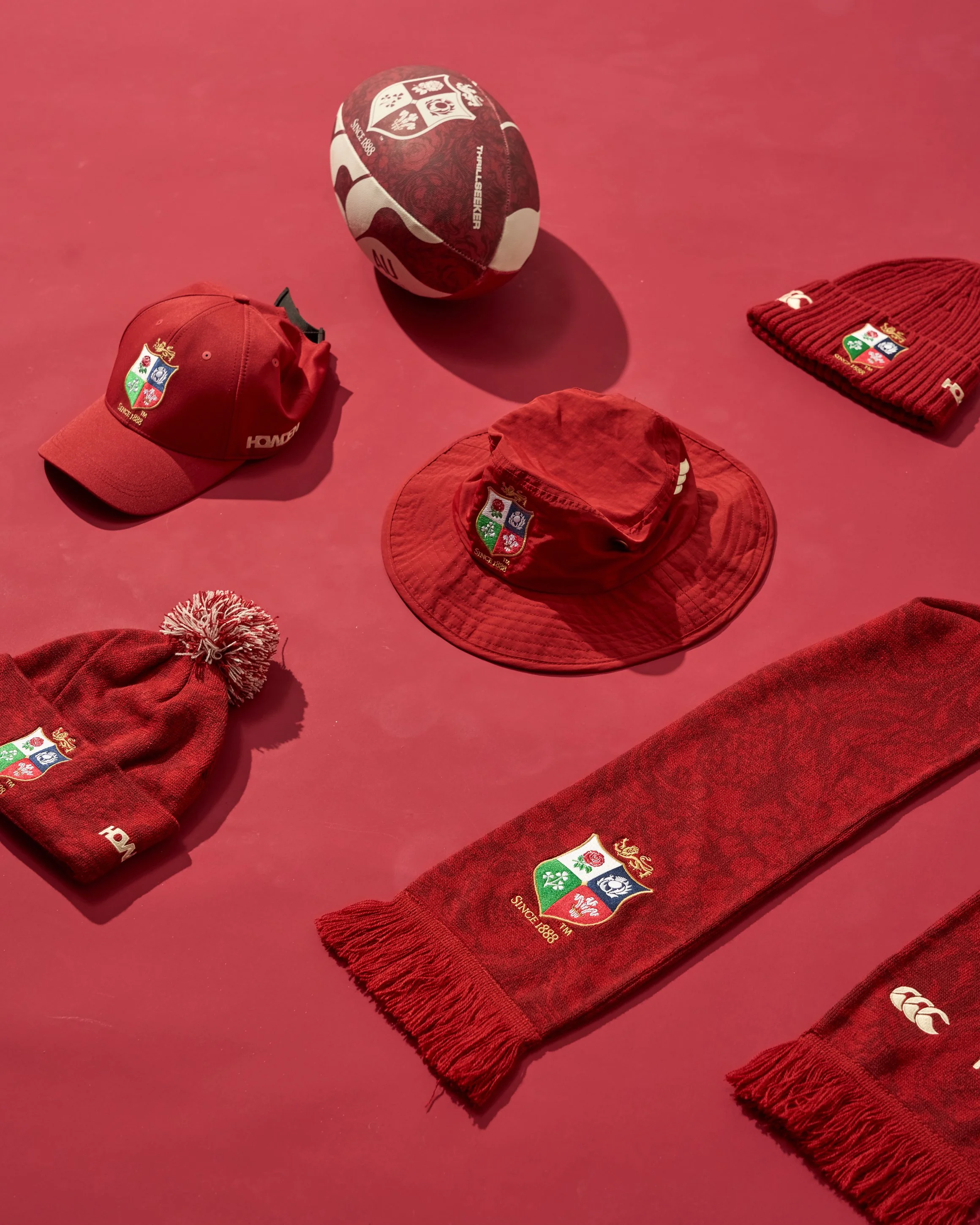 Various red sports accessories including caps, beanie, a scarf, and a ball, all displaying the Welsh Rugby Union crest.