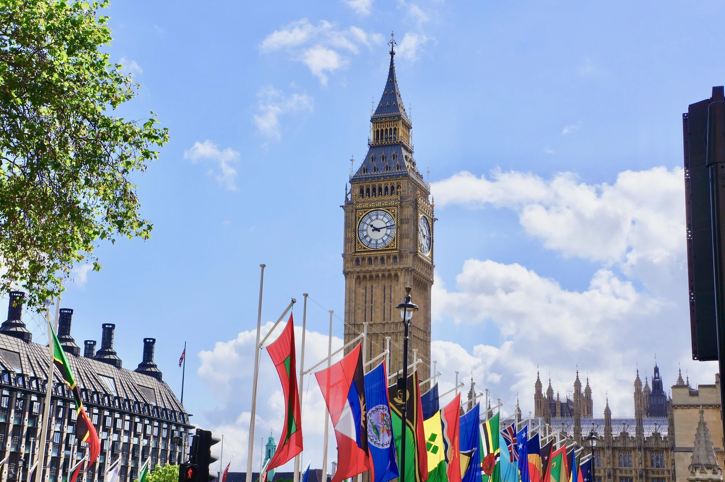 Big Ben clock tower with flags in London, blue sky and clouds.