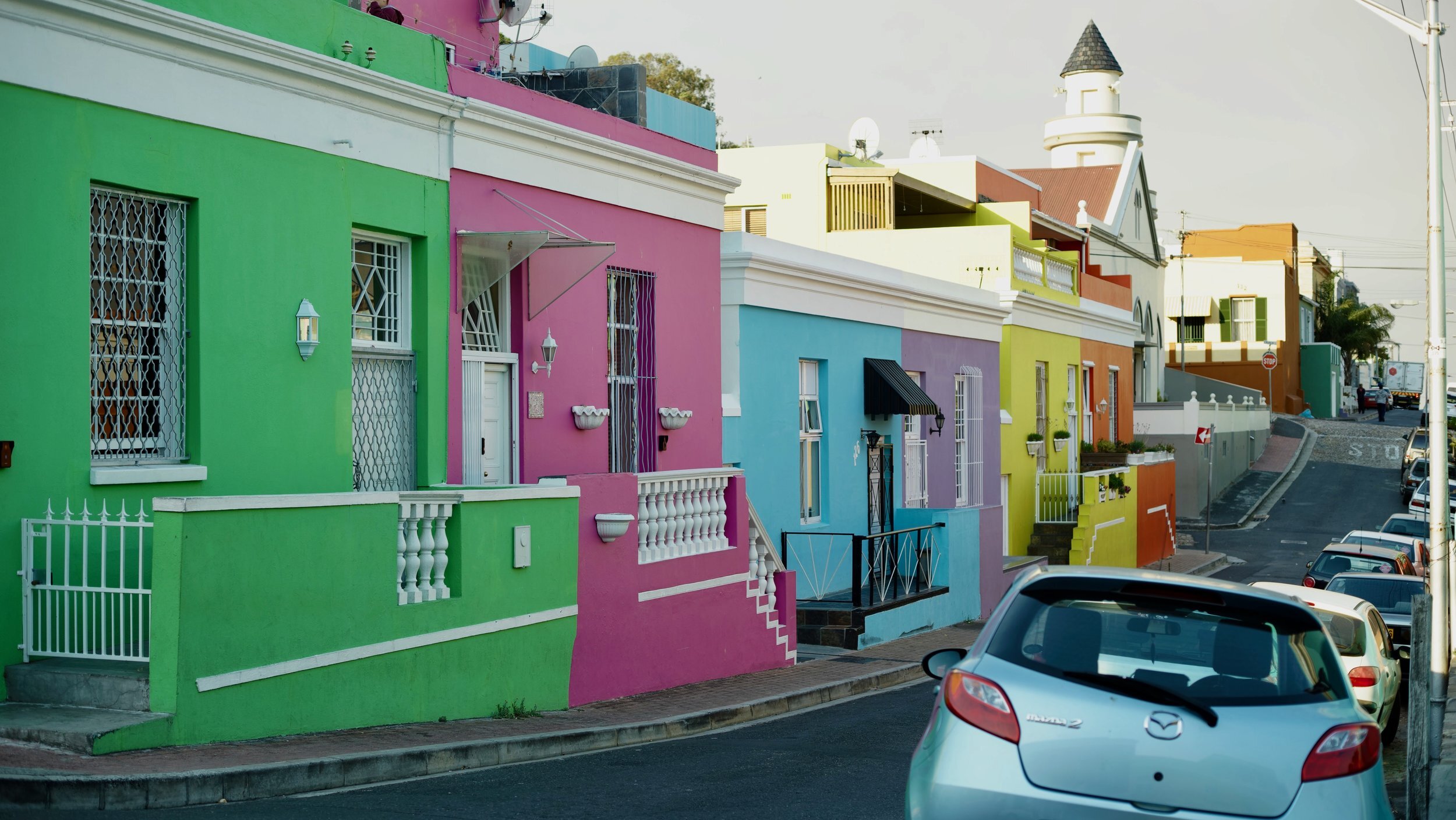 Colorful houses on a street with a parked car and a clear sky.