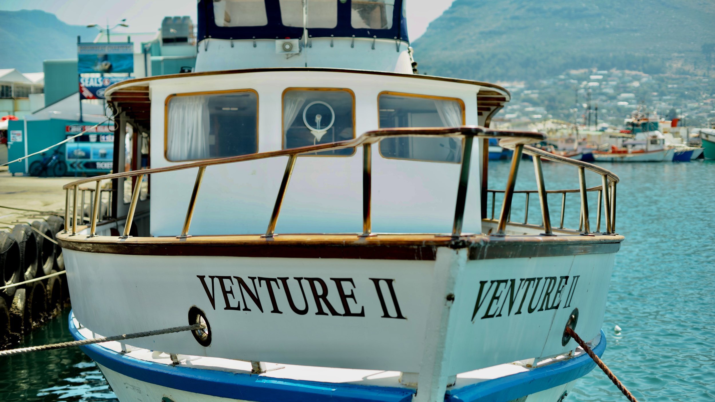 Front view of a boat named 'Venture II' docked at a harbor, with other boats and buildings in the background.