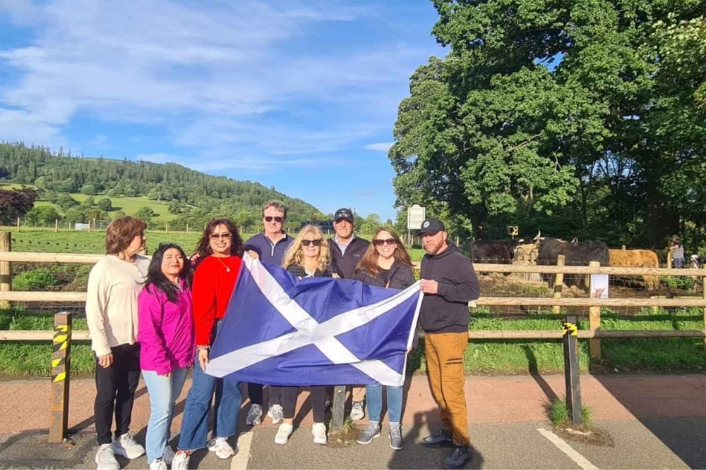 A tour group with a Saltire beside Highland cows