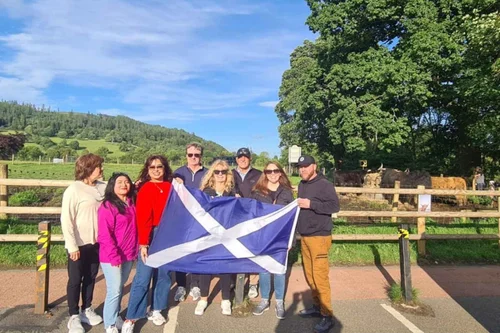A tour group with a Saltire beside Highland cows