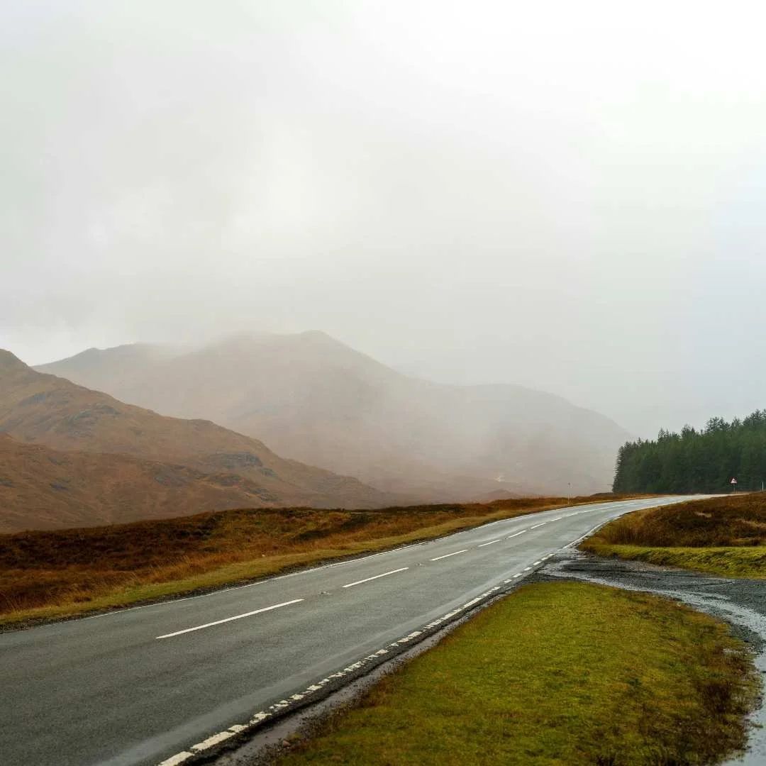 A quiet Scottish road disappearing towards hills in rain and low cloud