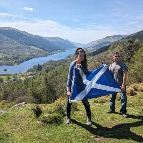 Travellers holding a Scottish flag above a Highland loch on a private tour