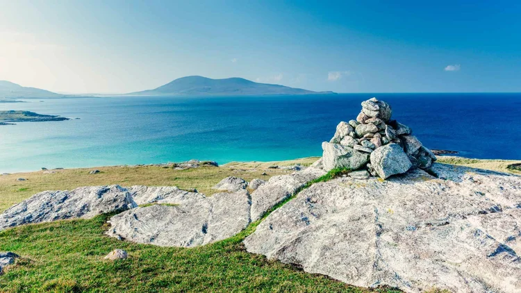 A stone cairn above turquoise water and white sand in the Outer Hebrides, on the 3-day Lewis & Harris tour from Inverness