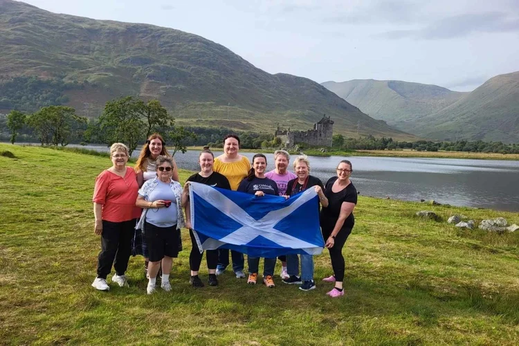 A tour group with a Scottish flag beside Loch Awe near Kilchurn Castle