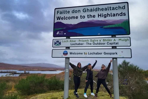 Three guests posing at a Welcome to the Highlands sign