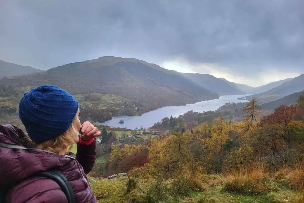 A traveller in a woolly hat looking out over a Highland loch and autumn hills