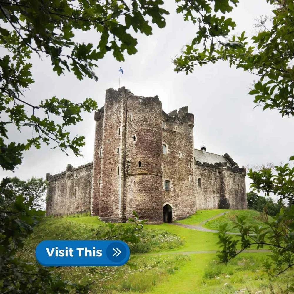 Doune Castle seen across a grassy field through the trees
