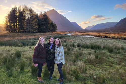 Three smiling travellers with Glencoe's mountains behind them