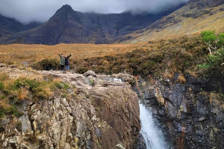 Two guests waving at the Fairy Pools with the Cuillin behind