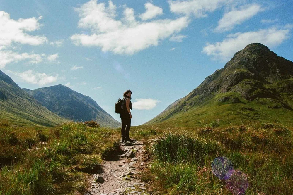 A walker on a path between green mountains in Glencoe