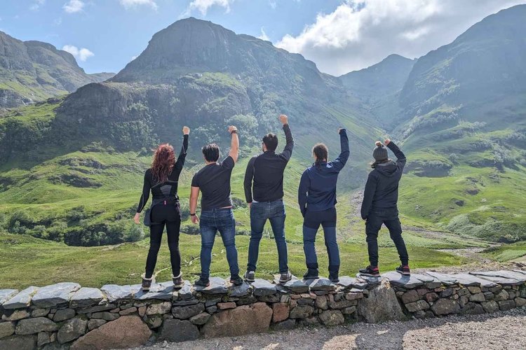 A tour group raising their fists towards Glencoe’s Three Sisters