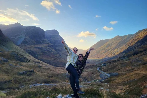 Two smiling travellers waving in Glencoe