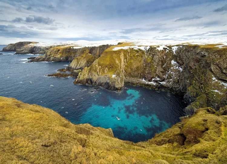 Sea cliffs and a turquoise inlet on the Shetland coast