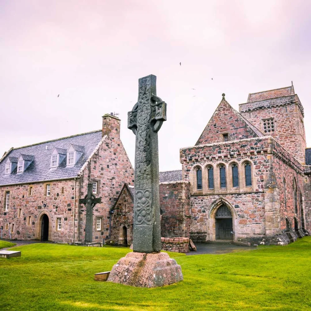 A carved stone cross in front of the stone buildings of Iona Abbey