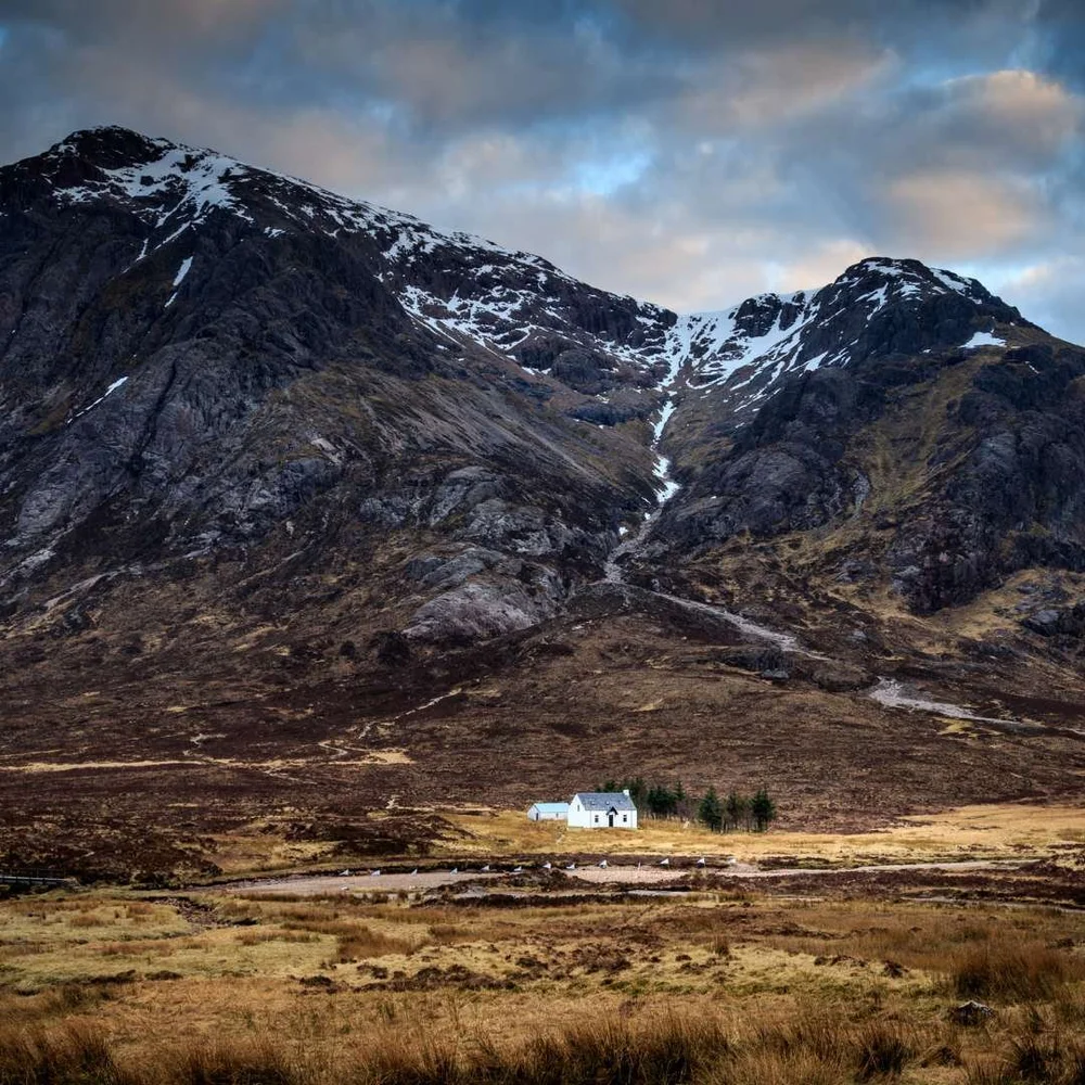 Snow-dusted mountains above a white cottage in Glencoe
