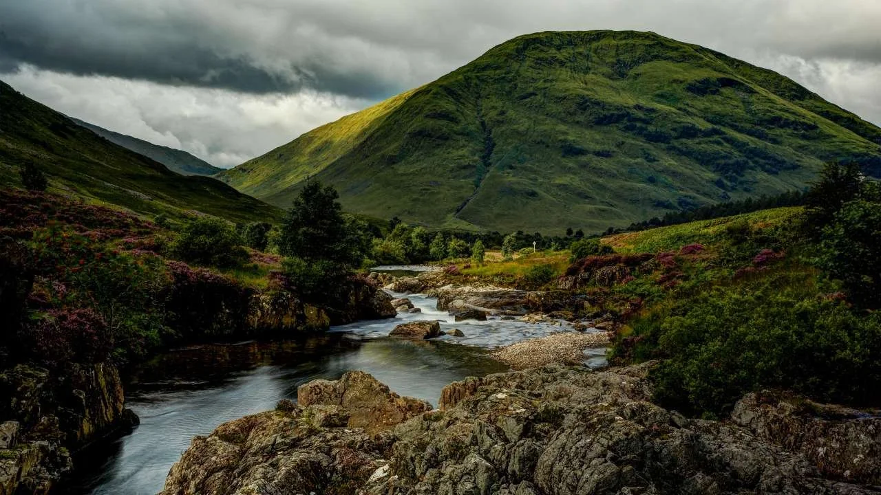 A Highland river beneath green mountains and gathering cloud