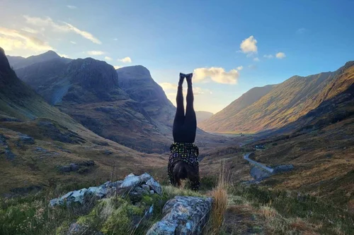 A traveller doing a handstand in front of Glencoe's mountains