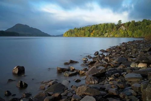 The rocky shore of Loch Laggan with autumn woods and hills beyond