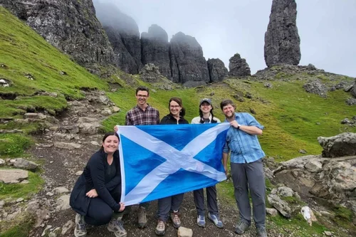 A small tour group with a Saltire below the Old Man of Storr