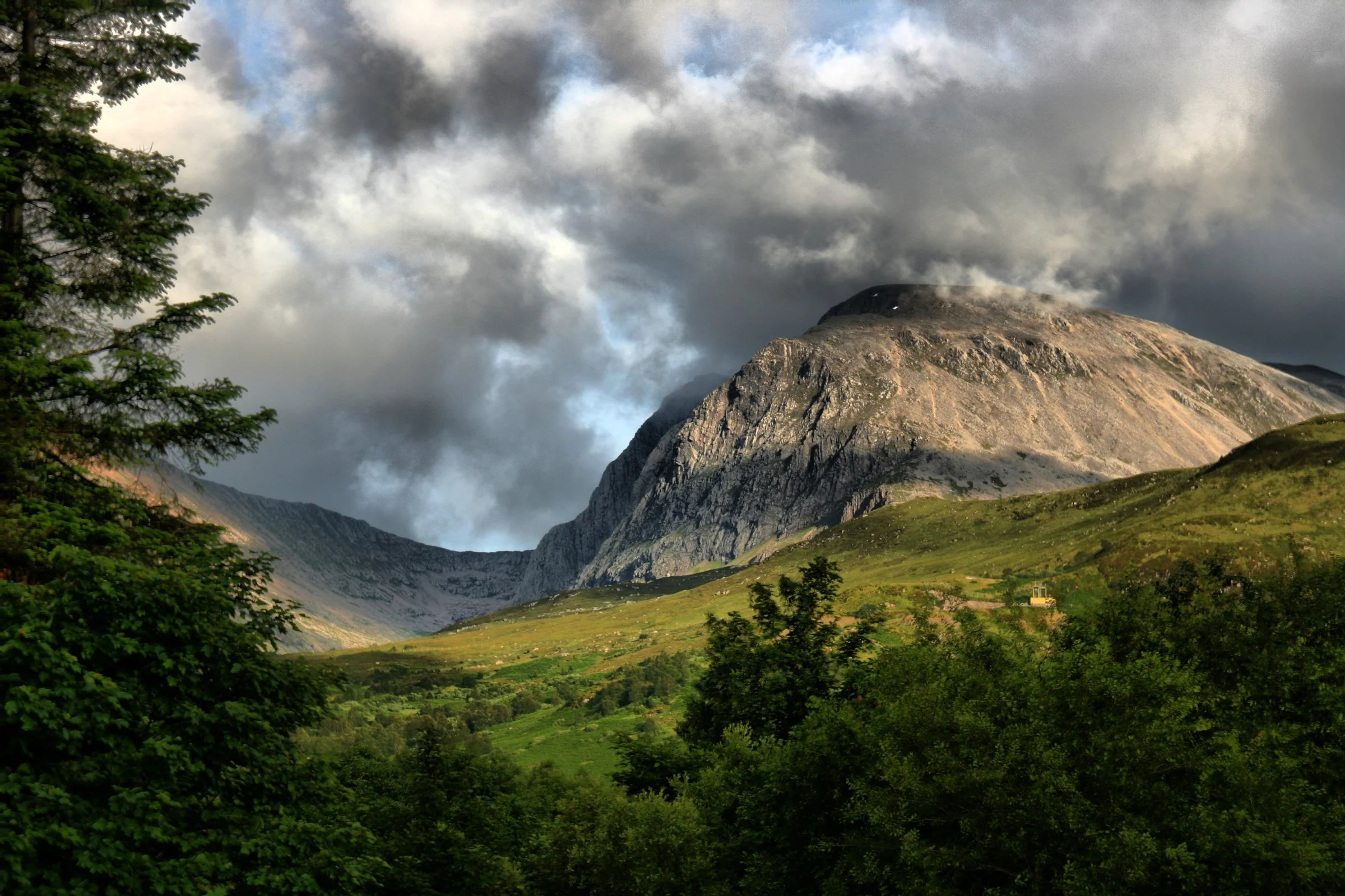 Ben Nevis rising above woodland beneath dramatic cloud