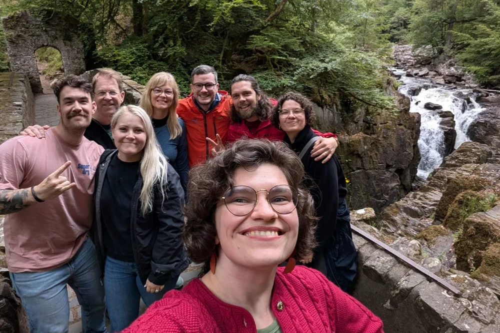 Scotland's Wild guides and guests smiling together beside a woodland waterfall