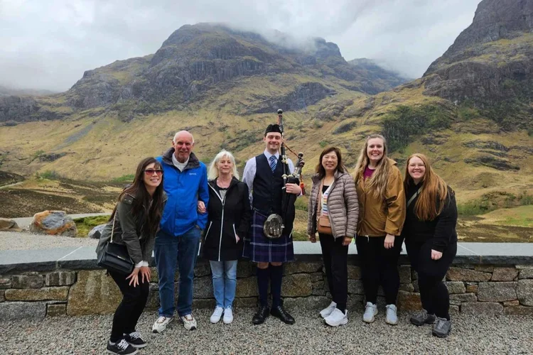 A piper playing for a tour group in Glencoe