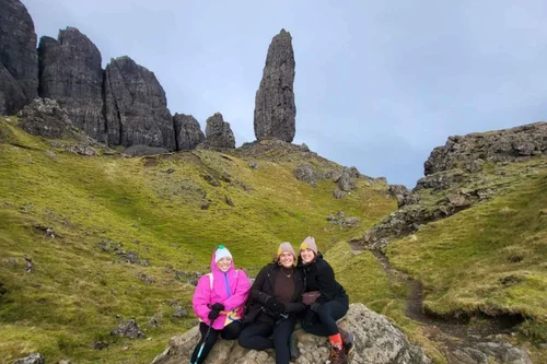 Three guests smiling with the Old Man of Storr behind them