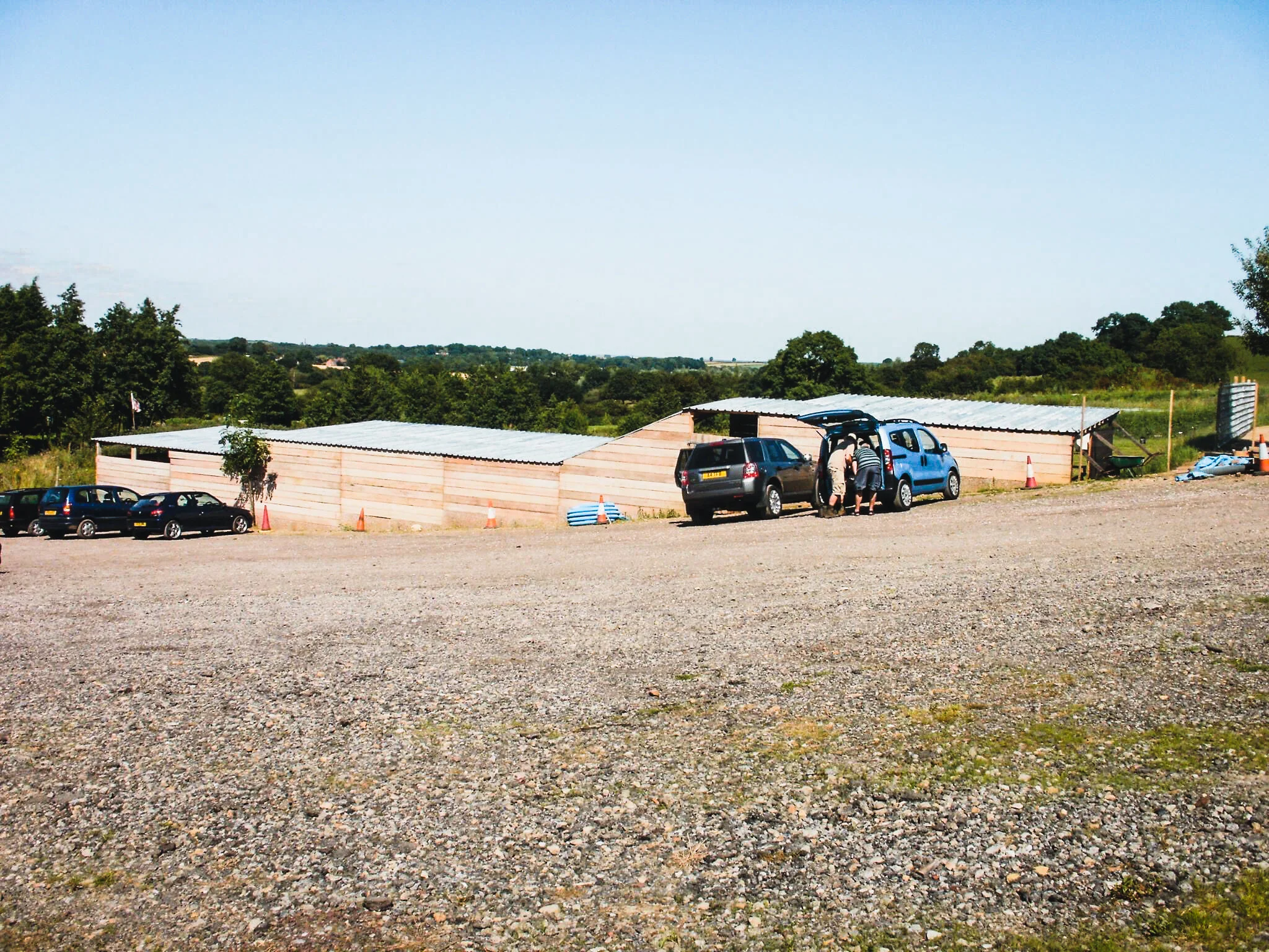 Cars parked on a gravel lot near a wooden structure under a clear sky