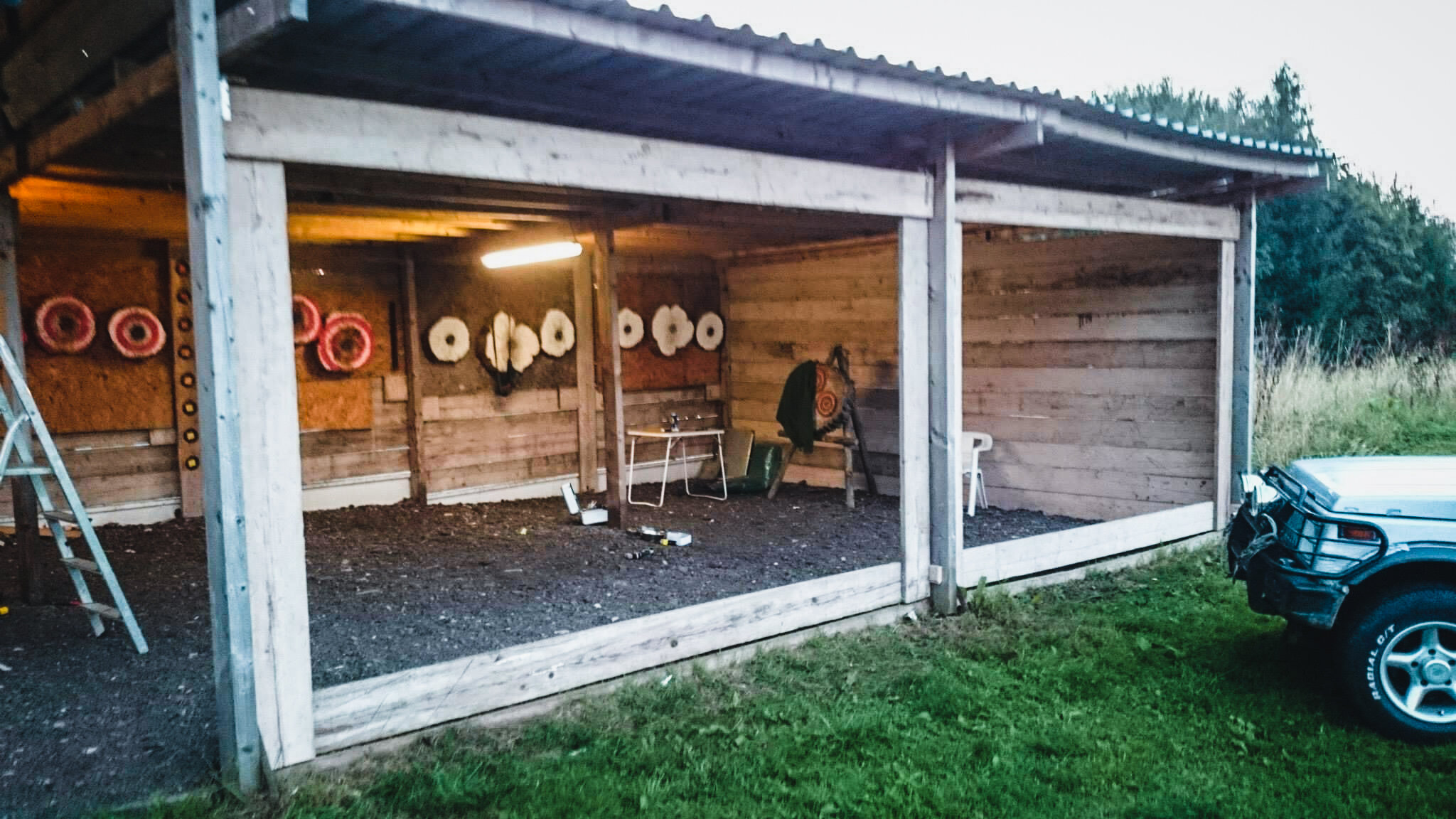 An outdoor archery range with targets on wooden walls and a car parked nearby.