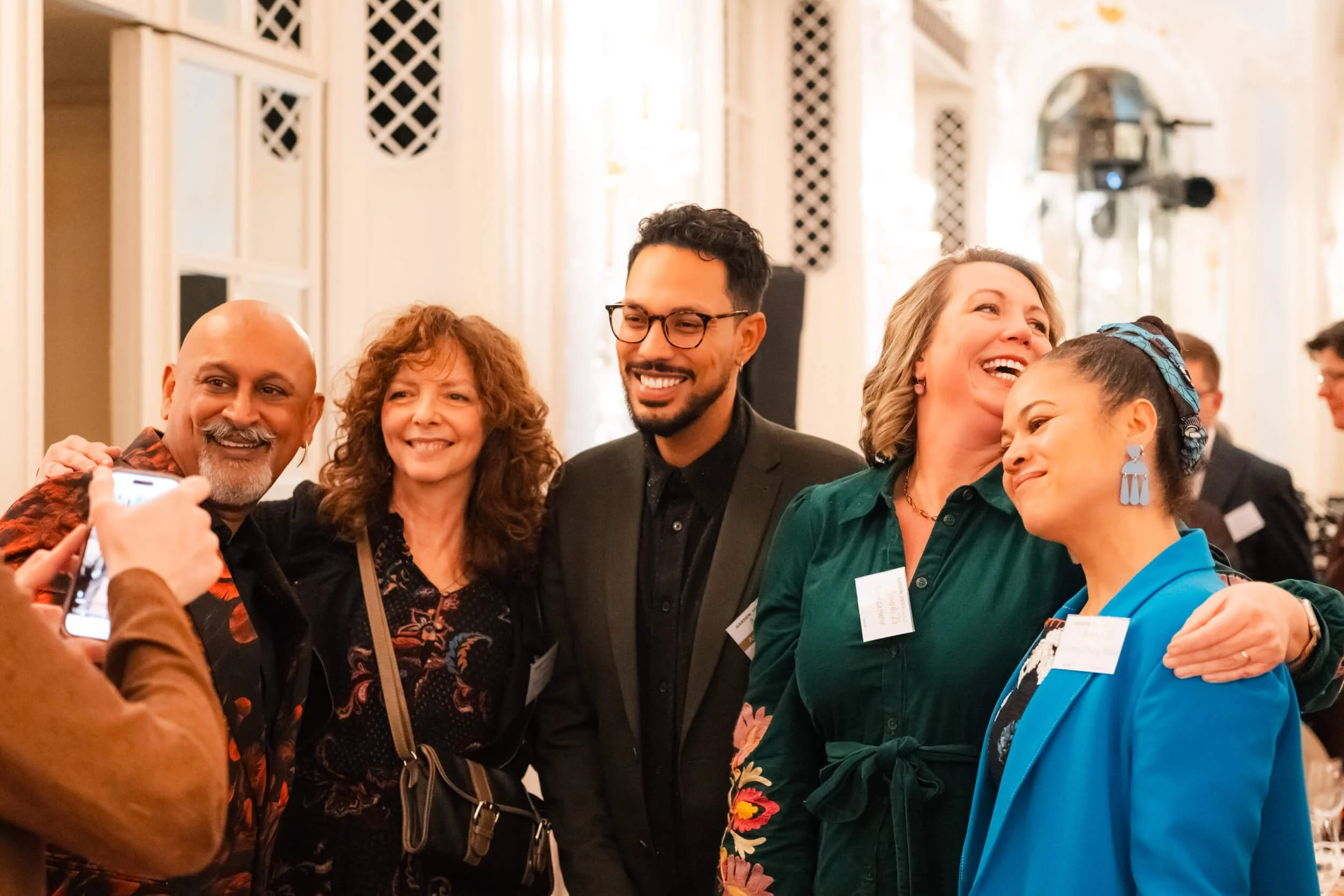 Group of five diverse people posing for a photo and smiling at an indoor event.