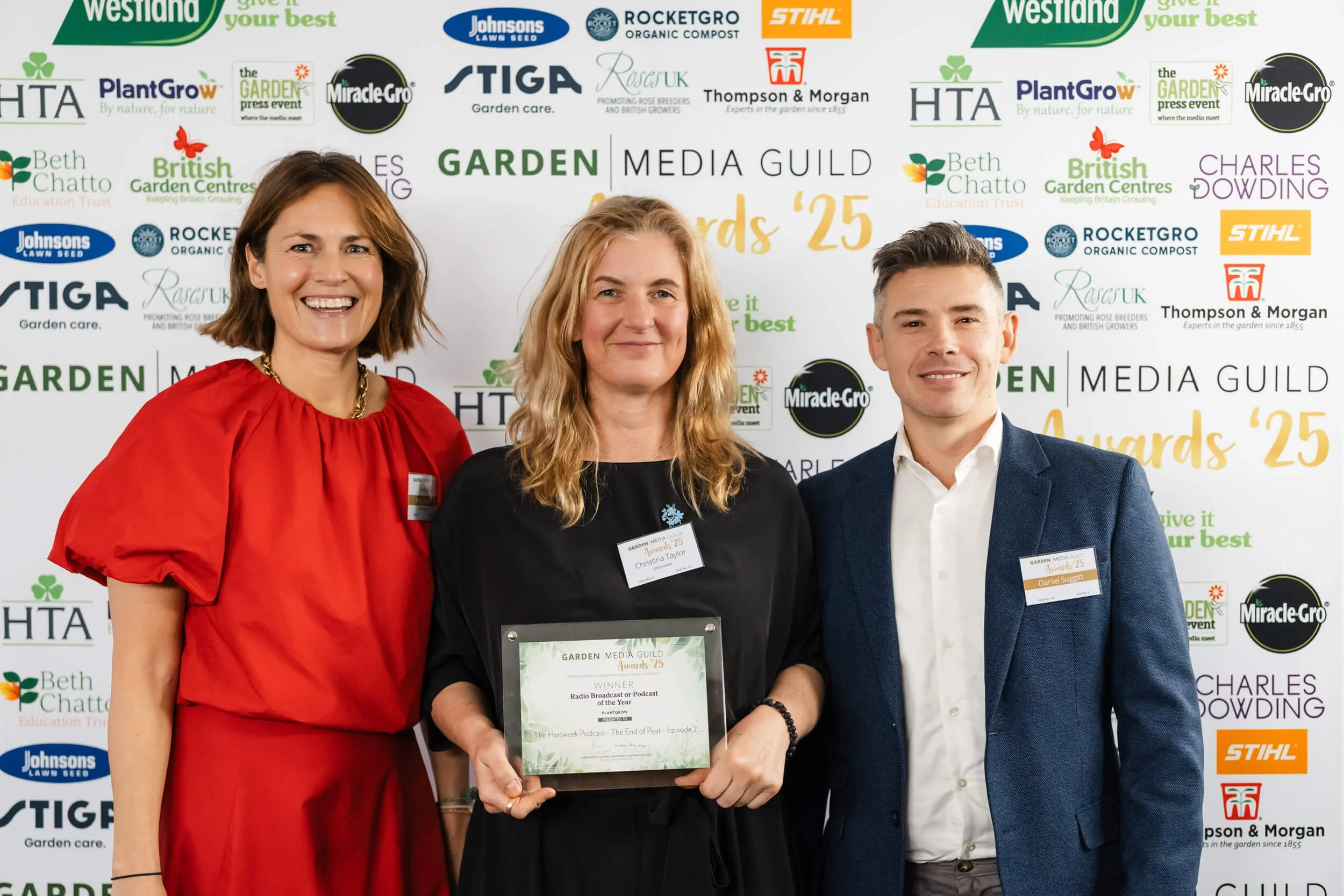 Three people standing together at an awards event, with two women and one man, smiling for the photo, holding a plaque. The backdrop features various gardening and media company logos and the text 'Awards '25'.