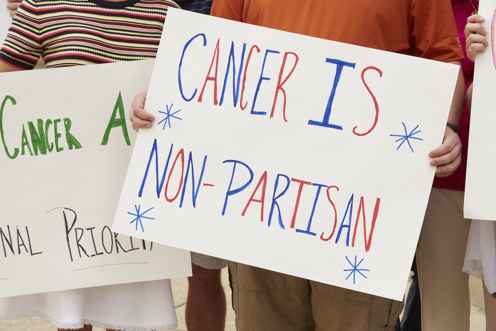 A sign that says "cancer is non-partisan" in red and blue colors