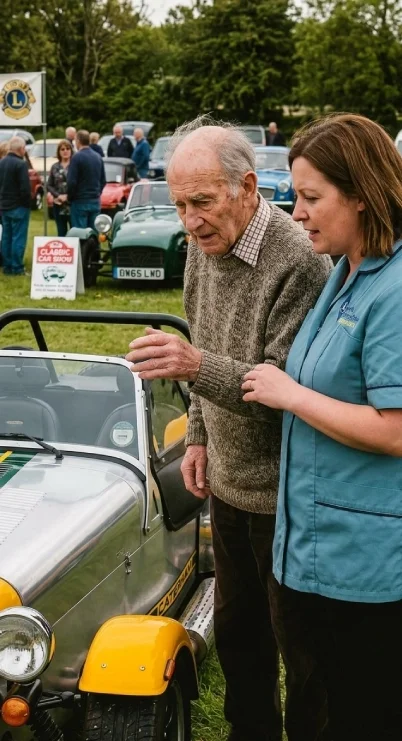 An elderly man and a woman in a blue shirt examining a vintage yellow and green car at an outdoor classic car show with other cars and people in the background.