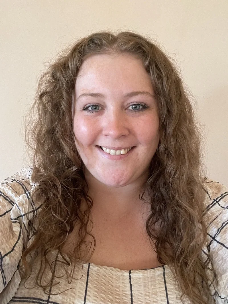 A woman with long, curly, light brown hair smiling at the camera. Alice Allen Deputy Manager
