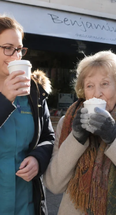 A young woman and an elderly woman are enjoying hot beverages outside, with a sign that says 'Benjamin...' in the background.