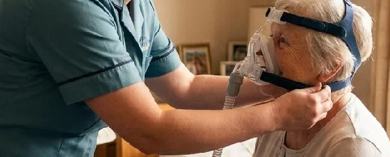 A healthcare worker assisting an elderly person with a sleep apnea mask.