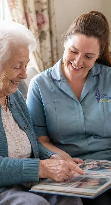 A young caregiver showing photo album to an elderly woman in a cozy home setting.