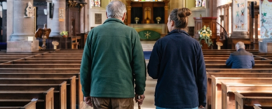 A man and woman walking inside a church, facing towards the altar.