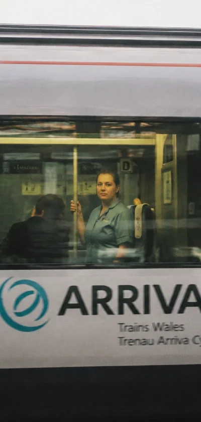A woman looking out from a train window with the Arriva logo, indicating a train in Wales, with reflections of the station visible on the glass.