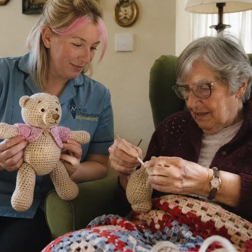 A young woman and an elderly woman are sitting together on a couch, engaging in knitting. The young woman is holding a crocheted teddy bear, while the elderly woman is knitting with yarn.