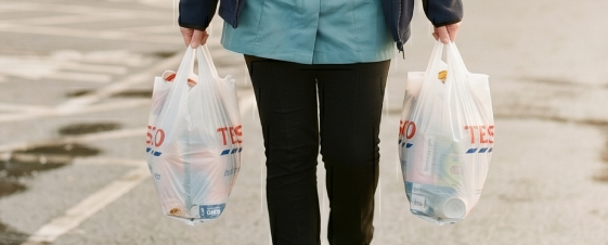 Person carrying two grocery bags in a parking lot.
