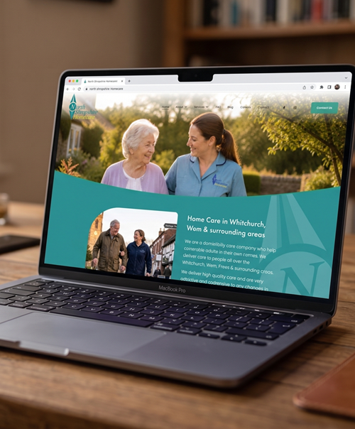 Laptop screen displaying a website for a home care service in Whitchurch, with images of elderly women and caregivers, on a wooden desk.