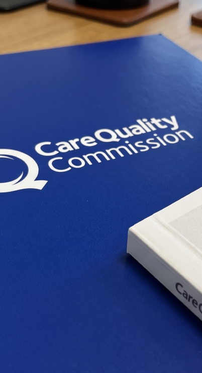 Care Quality Commission binder and a white box on a wooden table.