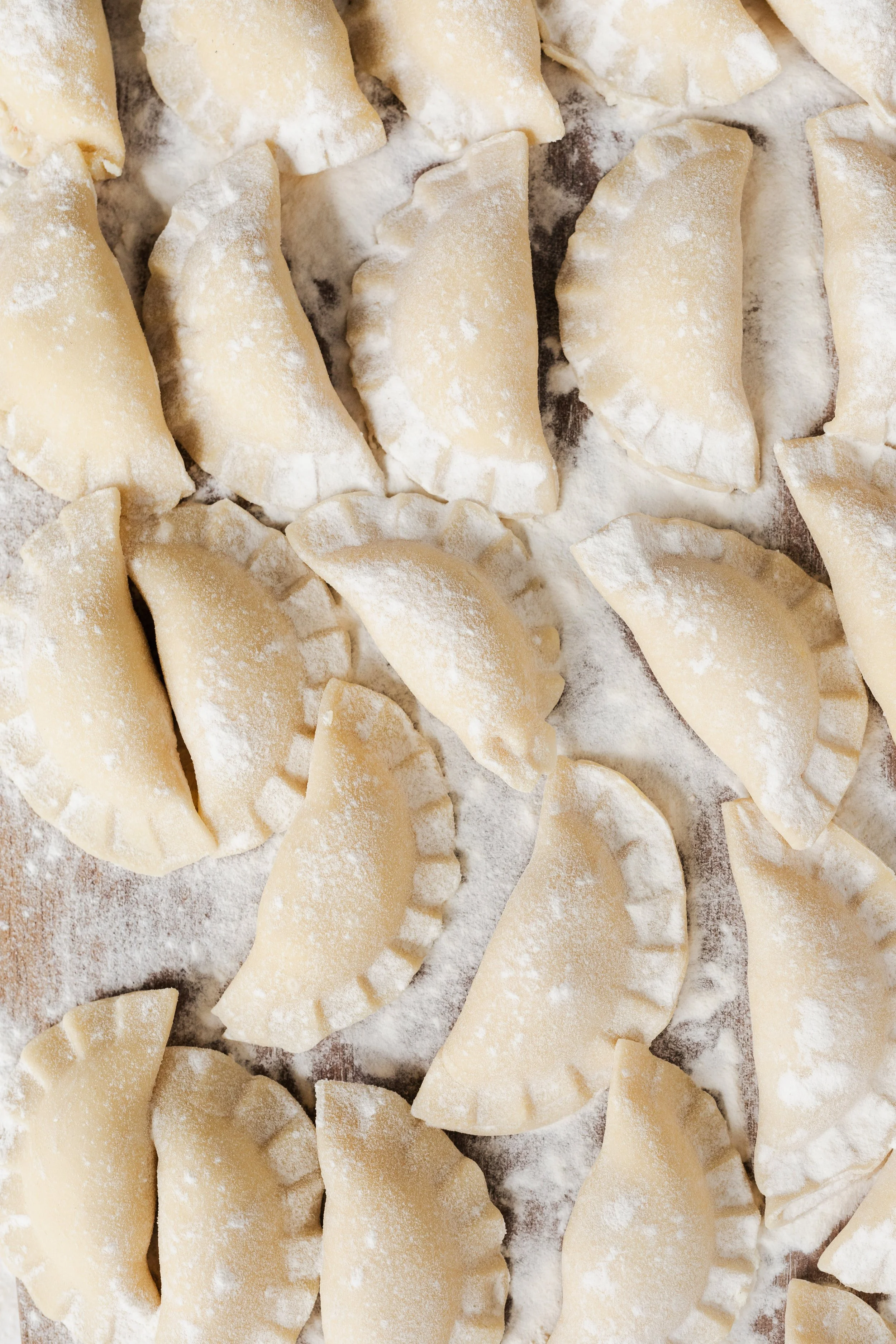 Uncooked, folded, and floured dumplings or pierogis arranged on a floured surface.