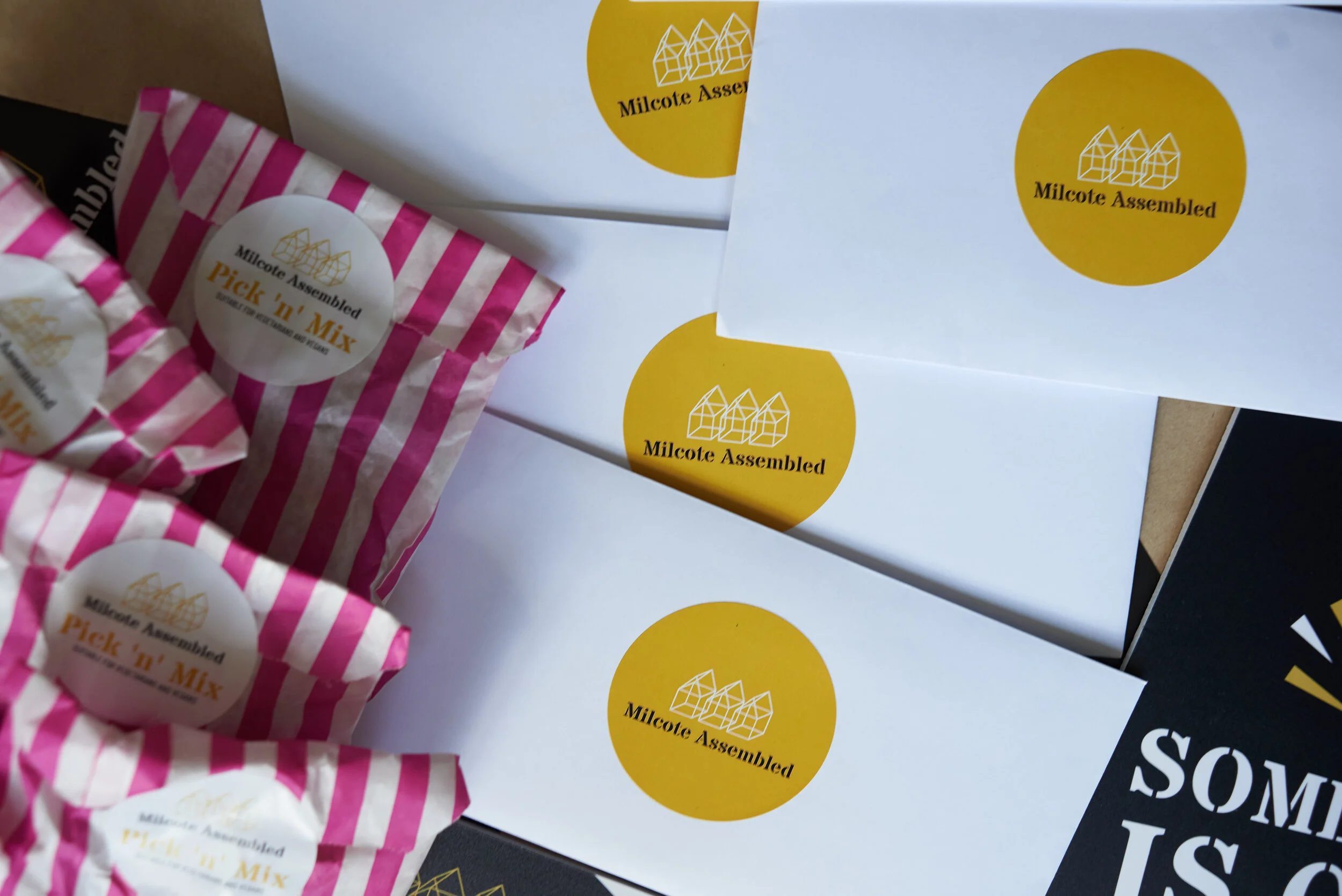 Multiple white envelopes with yellow circular logos reading 'Milcote Assembled,' some with pink and white striped packaging of a product labeled 'Pick 'n' Mix,' placed on a flat surface.